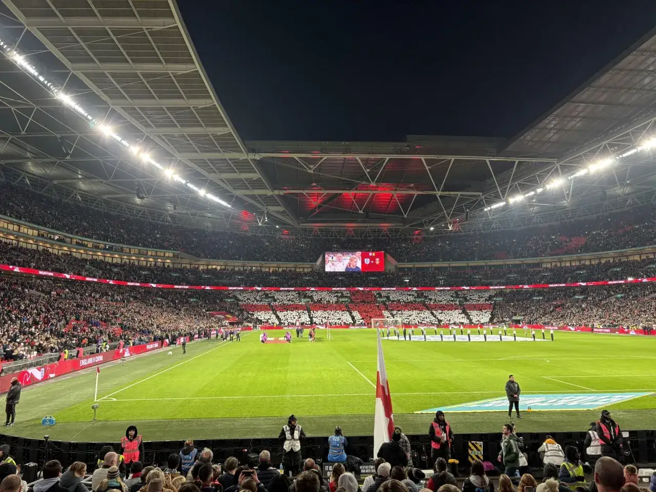 Stadion pełen kibiców podczas meczu ligi angielskiej. Na murawie zielona trawa, a nad nią rozświetlony dach.