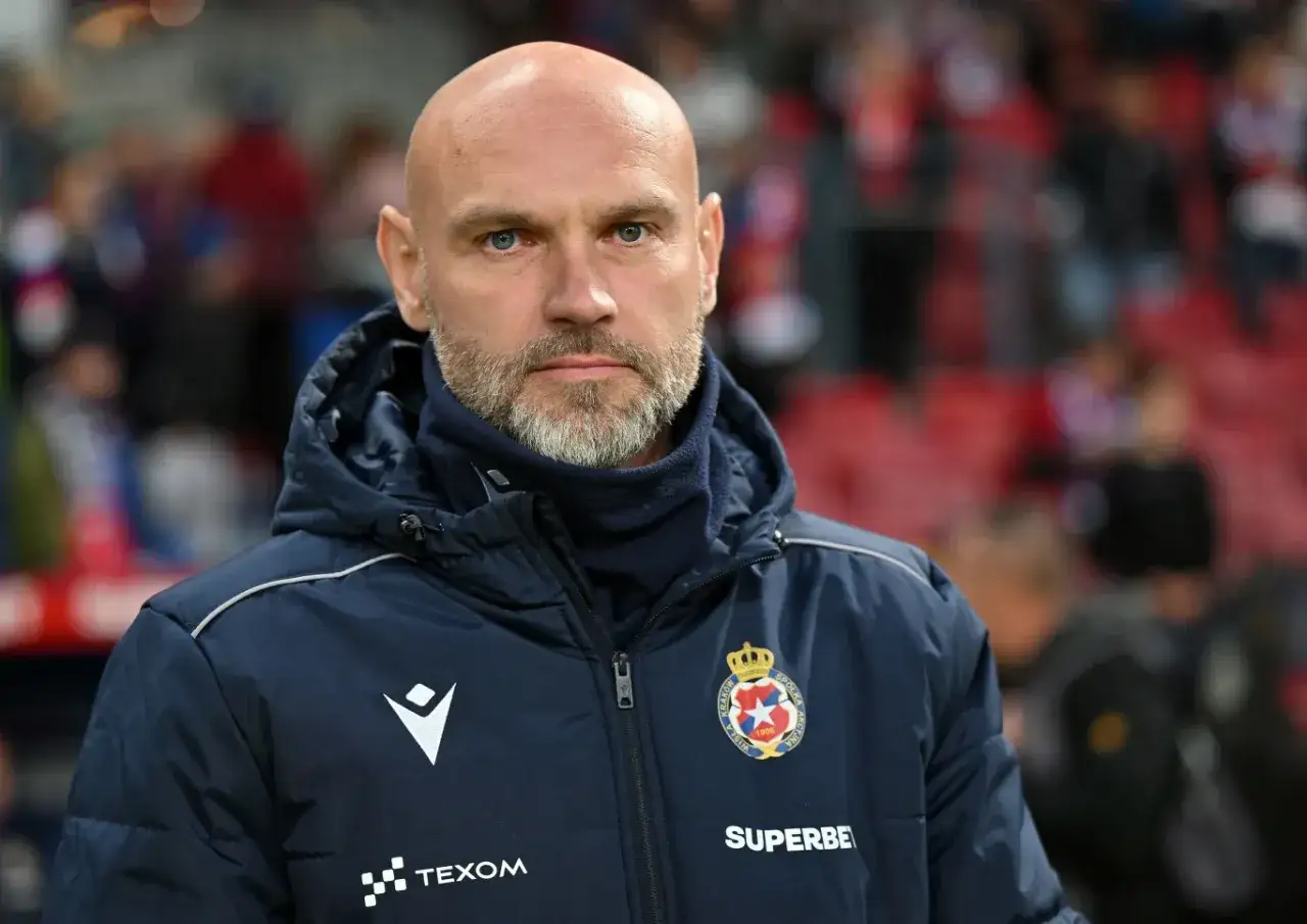 Łysy mężczyzna z brodą, trener Wisły Kraków, w granatowej kurtce z herbem klubu.
