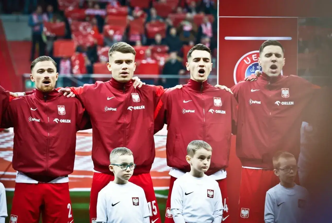 Zgrupowanie reprezentacji Polski. Piłkarze w czerwonych dresach z orłem na piersi, obok nich dzieci w białych koszulkach.