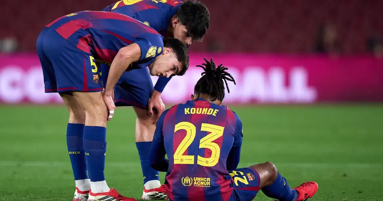 Piłkarze FC Barcelona zmartwieni po kontuzji kolegi. Koundé siedzi na murawie, koledzy pochylają się nad nim.
