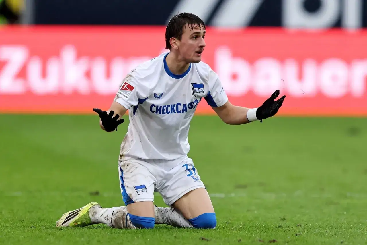 Piłkarz Herthy BSC, jeden z zawodników 2. Bundesligi, klęczy na boisku, wyrażając frustrację.