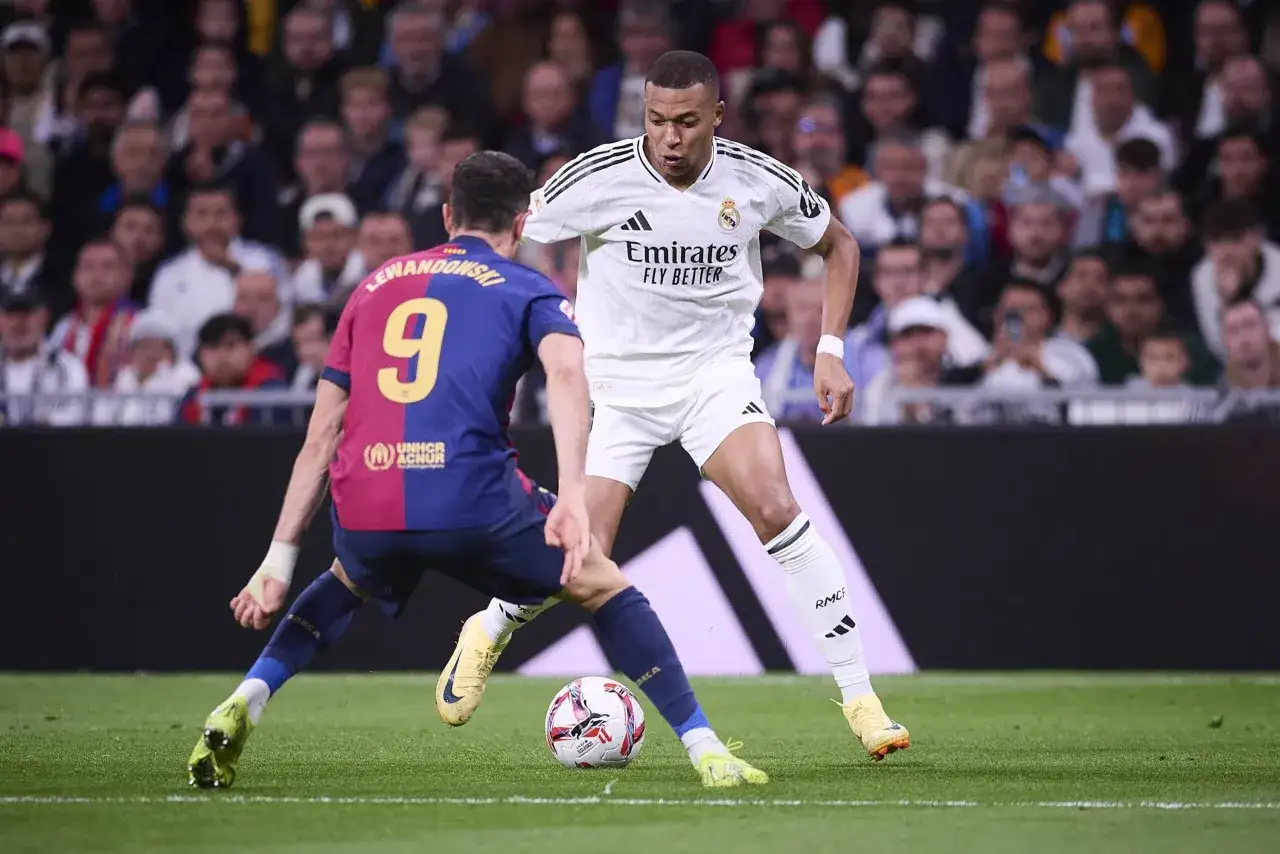 Mbappé w białej koszulce Realu Madryt walczy o piłkę z Lewandowskim w bordowo-granatowej koszulce Barcelony. Obaj są czołowymi strzelcami La Liga.