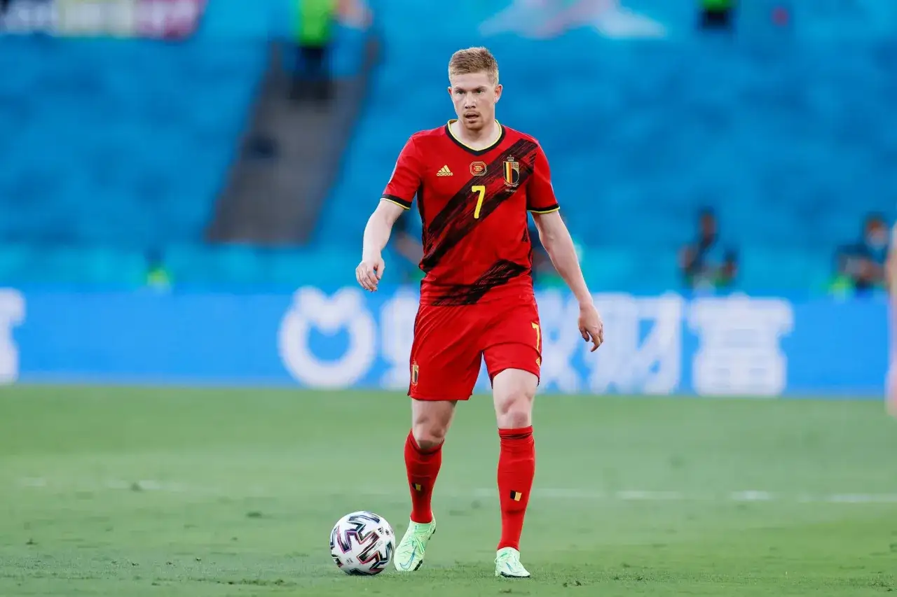 Kevin De Bruyne w czerwonej koszulce z numerem 7, z piłką przy nodze na boisku.