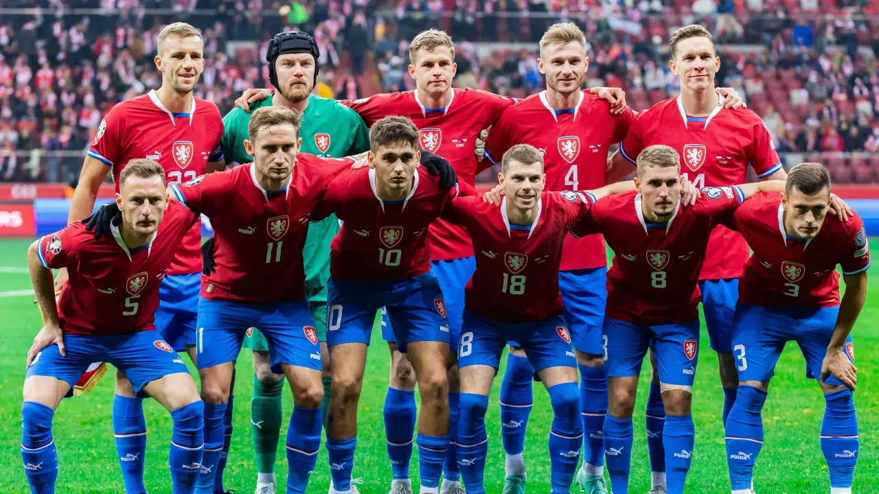 Drużyna piłkarska Czechów w czerwonych strojach, gotowa do gry. Każdy czeski piłkarz prezentuje determinację na twarzy.