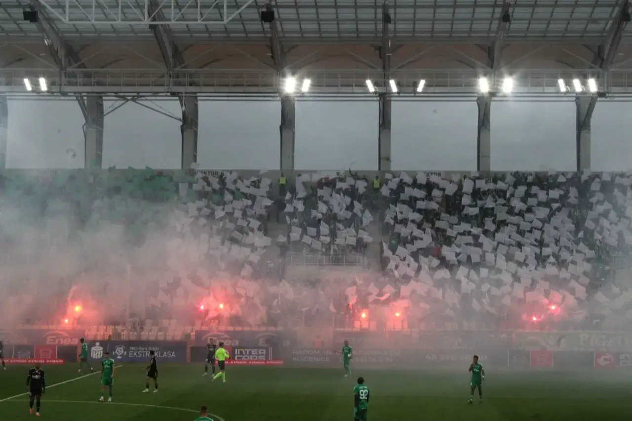 Tłum ultrasi na trybunach macha białymi flagami, a stadion spowija dym z rac.