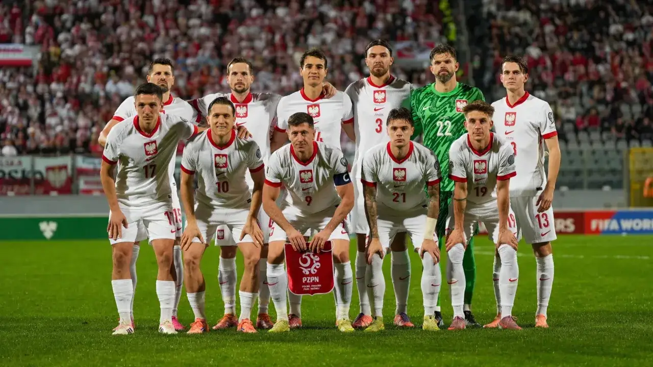 Piłkarze reprezentacji Polski w białych strojach pozują do zdjęcia na tle trybun.