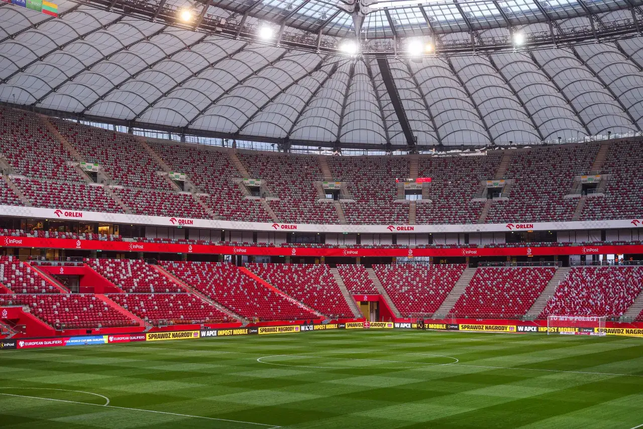Pusta trybuna stadionu przed meczem mistrzostwa polski w piłce nożnej. Czerwono-białe krzesełka czekają na kibiców.