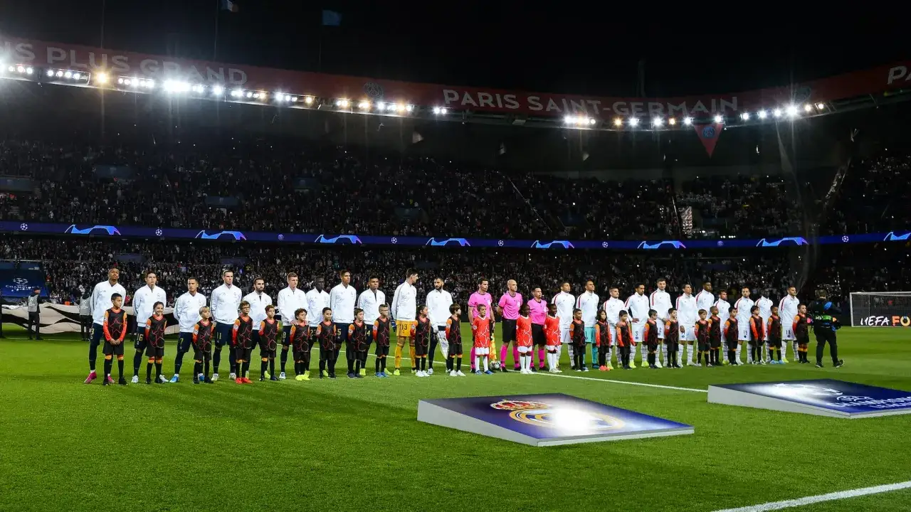 Piłkarze i dzieci stoją na murawie stadionu przed meczem Ligi Mistrzów, słychać hymn.
