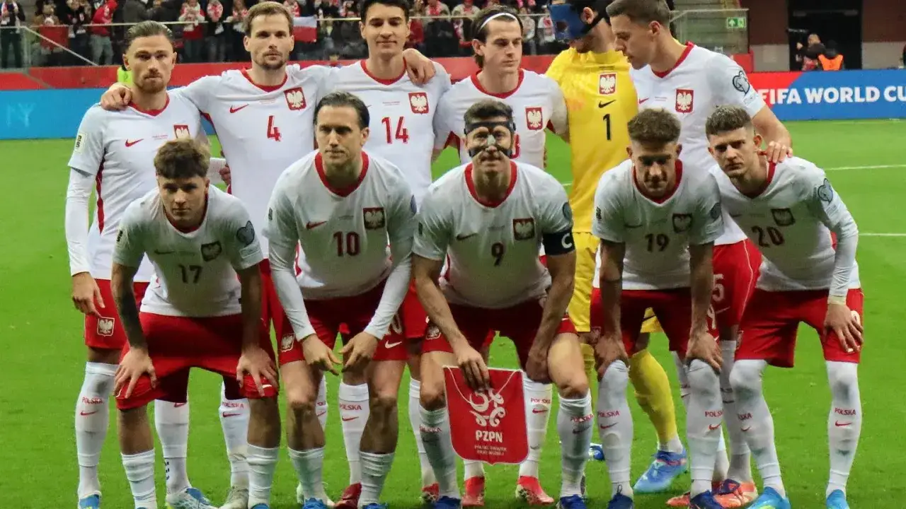 Drużyna piłkarska Polska w białych strojach z orłem na piersi. Piłkarze pozują do zdjęcia przed meczem.
