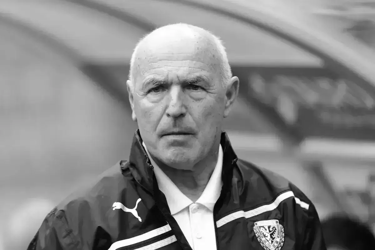 Portret łysiejącego mężczyzny w czapce z daszkiem i kurtce sportowej. To lenczyk trener piłkarski, zdeterminowany i skupiony.