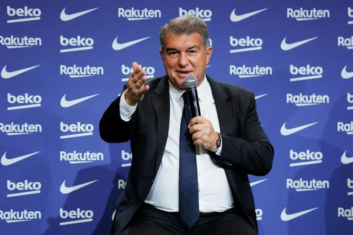 Prezes Barcelony, Joan Laporta, przemawia do mikrofonu na tle ścianki z logo klubu.