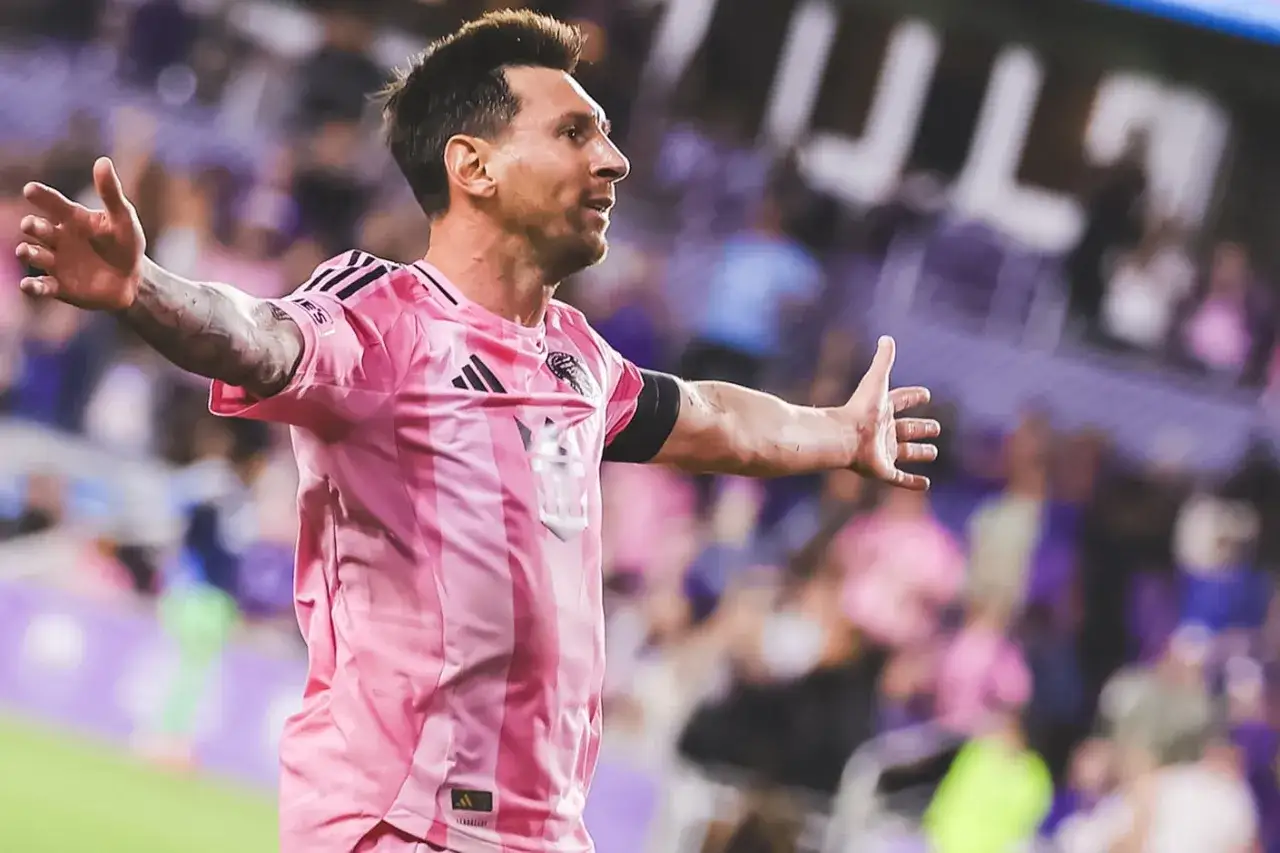 Leo Messi w różowej koszulce świętuje bramkę. Widać trybuny pełne kibiców. To właśnie tam gra Messi.